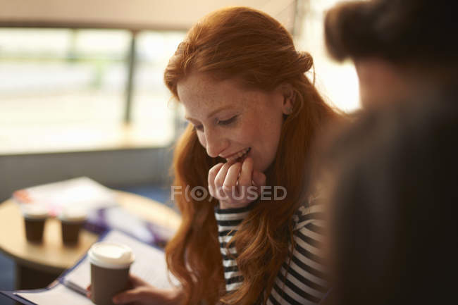 Mujer joven con lectura de café para llevar en la sala común - foto de stock