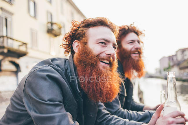 Gemelos hipster masculinos jóvenes con pelo rojo y barba en el paseo marítimo del canal - foto de stock