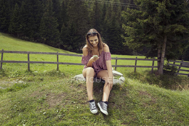 Jovem mulher sentada em campo lendo textos de smartphones, Sattelbergalm, Tirol, Áustria — Fotografia de Stock