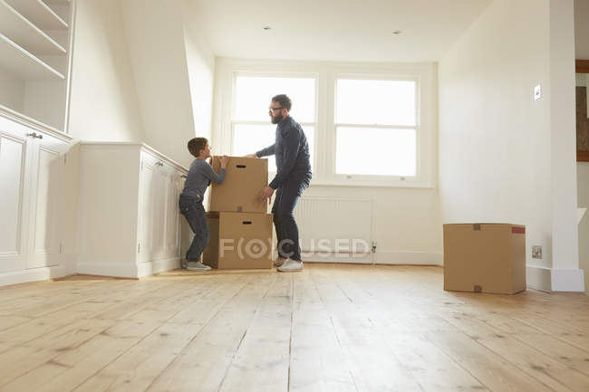 Mittlerer erwachsener Mann und Sohn stapeln Karton in neuem Zuhause — Stockfoto