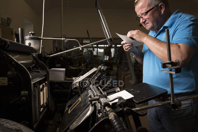 Imprimante mâle mature inspectant le papier pour les machines d'impression dans l'atelier de presse d'impression — Photo de stock