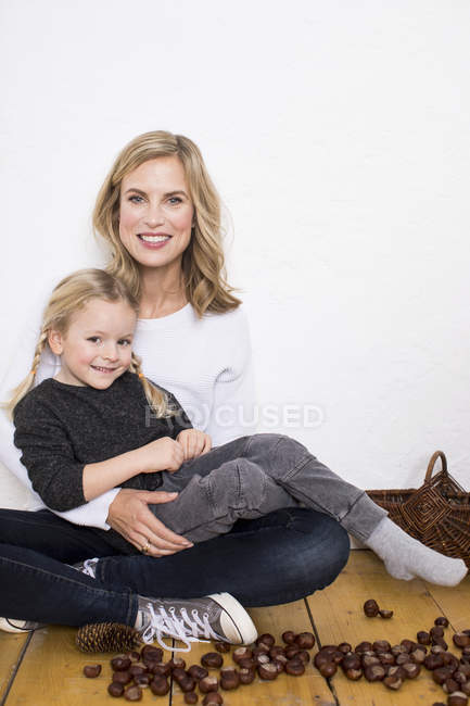 Portrait of mother and daughter, sitting on floor, surrounded by conkers and pine cones — Stock Photo