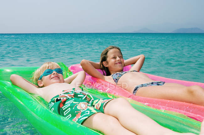 Девочка и мальчик на надувных матрацах в морской воде — стоковое фото