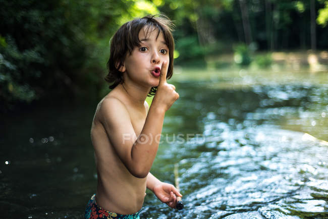 Boy waist deep in water with finger on lips — Stock Photo