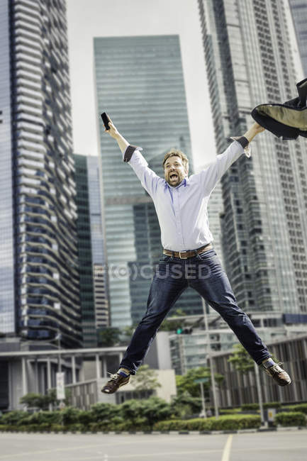 Heureux homme d'affaires sautant de joie près des gratte-ciel de la ville bâtiments — Photo de stock