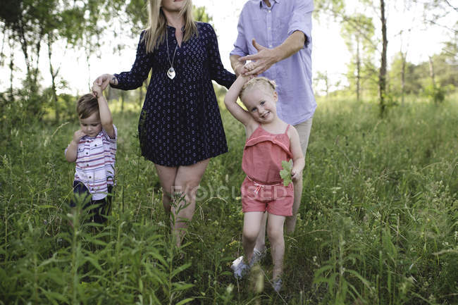 Mid adultos pais passeando no prado menino e menina — Fotografia de Stock