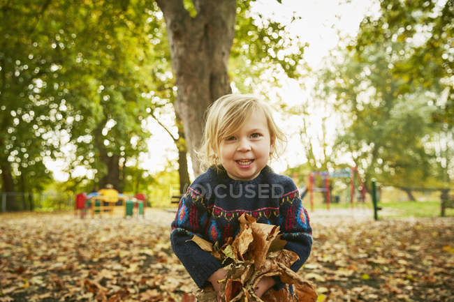 Ragazza sorridente che gioca in foglie di autunno — Foto stock