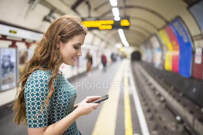 Seitenansicht einer Frau am Bahnsteig, die auf ihr Smartphone schaut — Stockfoto