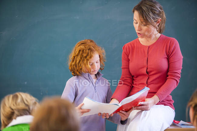 Primary schoolgirl reading book at front of classroom — Stock Photo