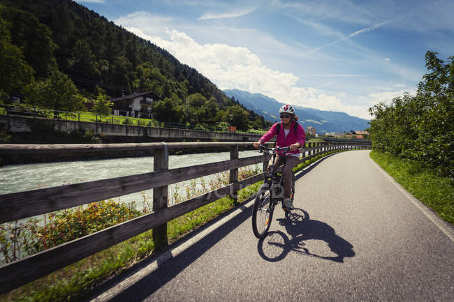 Female cyclist cycling along path by river in Vinschgau Valley, South Tyrol, Italy — Stock Photo