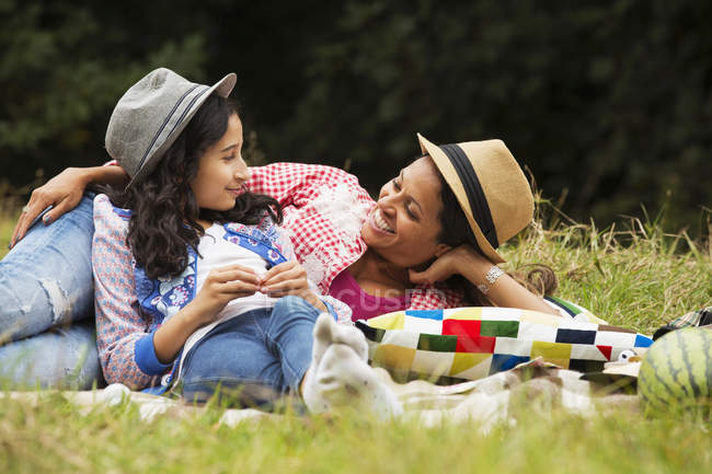 Madre e hija relajándose al aire libre, tumbadas en una manta de picnic - foto de stock