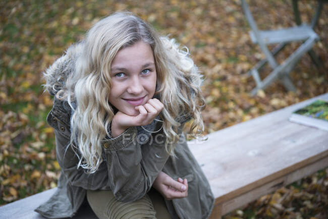 Ritratto di ragazza bionda seduta sulla panchina del giardino in autunno — Foto stock