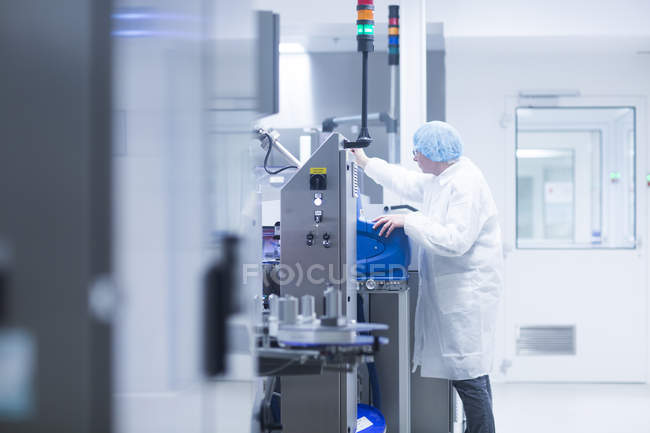 Trabajador operando maquinaria en línea de producción en planta farmacéutica - foto de stock