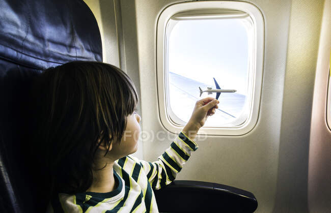 Chico jugando con juguete avión en avión ventana - foto de stock