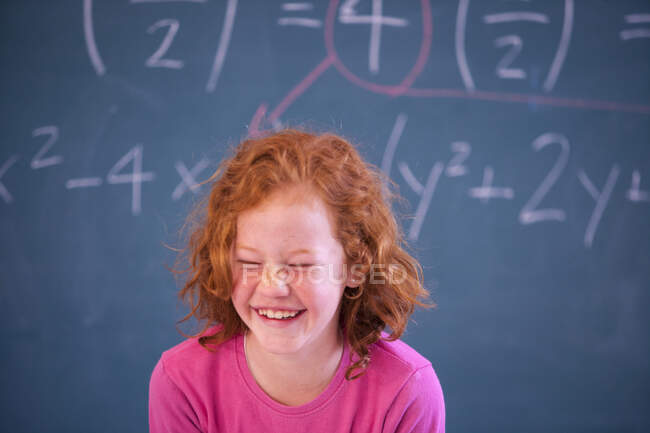 Retrato de linda colegiala primaria riéndose en el aula - foto de stock