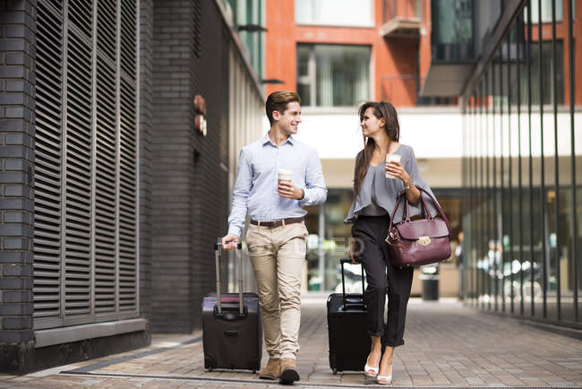 Young businessman and woman with wheeled suitcases walking and talking, London, UK — Stock Photo