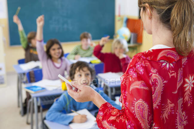 Over the shoulder view of primary school teacher questioning in classroom — Stock Photo