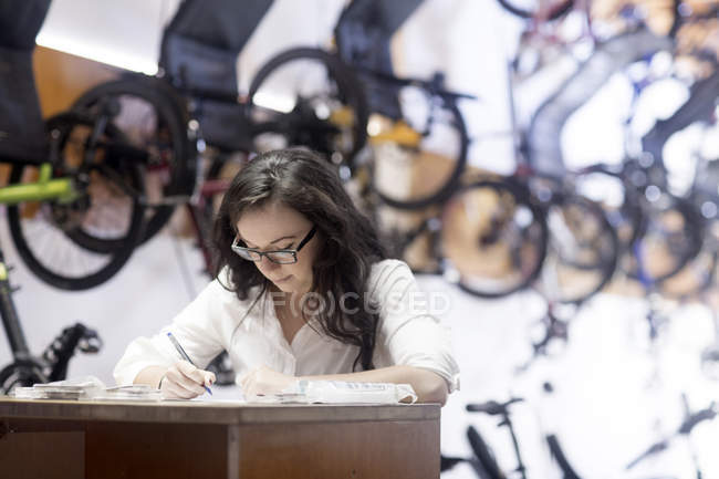 Mujer en la tienda de bicicletas trabajando en el mostrador - foto de stock