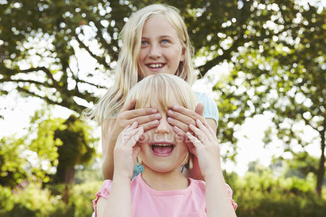 Girl with hands covering friend's eyes in garden — Stock Photo