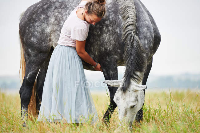 Woman in skirt with arms around dapple grey horse in field — Stock Photo