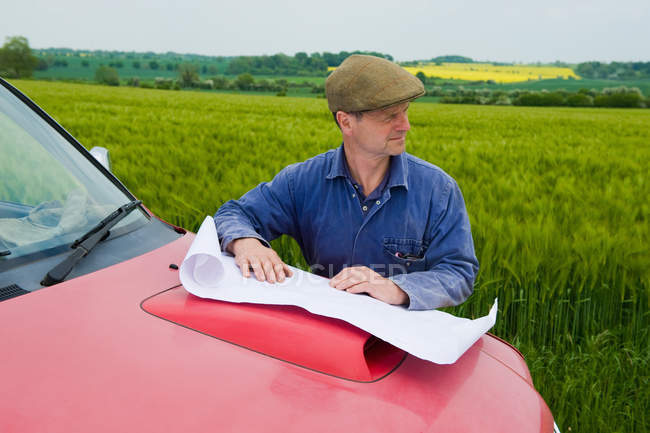 Farmer with blueprint on truck hood looking on field — Stock Photo