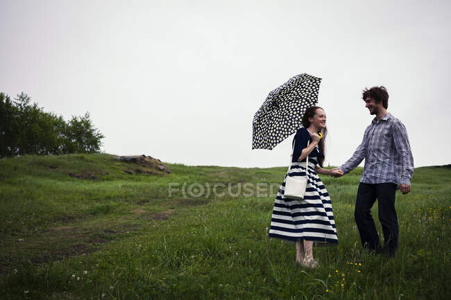 Пара, стоячи в полі, тримає руки, молода жінка тримає парасольку — стокове фото