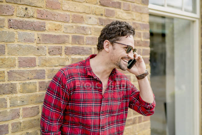 Young man in front of brick wall talking on smartphone — Stock Photo