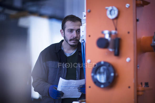 Young adult male Engineer holding paperwork operating control panel — Stock Photo