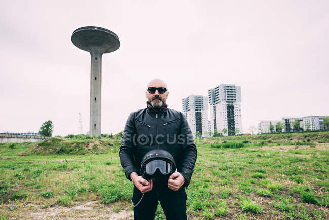 Портрет дорослого чоловіка мотоцикліста, що стоїть на пустирі, тримає шолом — стокове фото