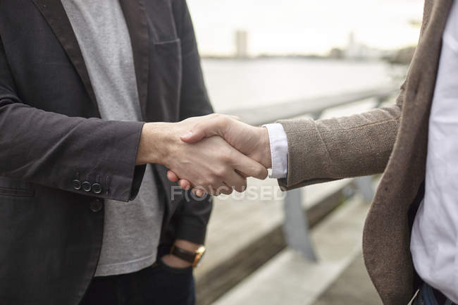 Vue médiane de deux hommes d'affaires serrant la main sur le front de mer, Londres, Royaume-Uni — Photo de stock