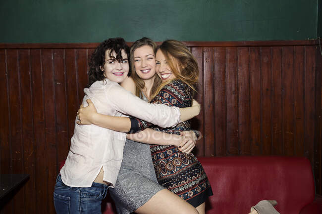 Three adult female friends having group hug in bar — Stock Photo