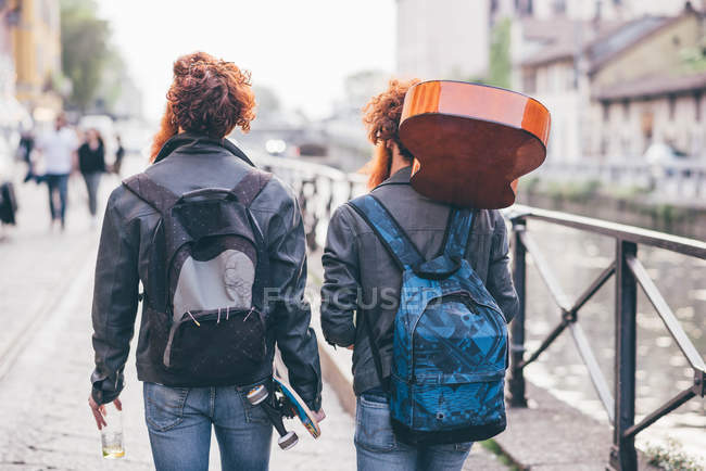 Вид сзади на молодых хипстерских близнецов с рыжими волосами, прогуливающихся вдоль берега канала — стоковое фото