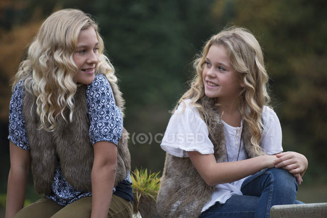 Two sisters sitting on patio table looking at each other — Stock Photo