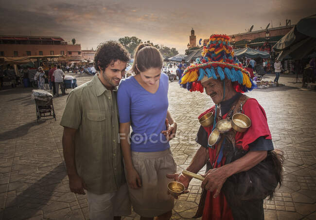 Coppia giovane che chiacchiera con il commerciante di mercato, Jemaa el-Fnaa Square, Marrakech, Marocco — Foto stock