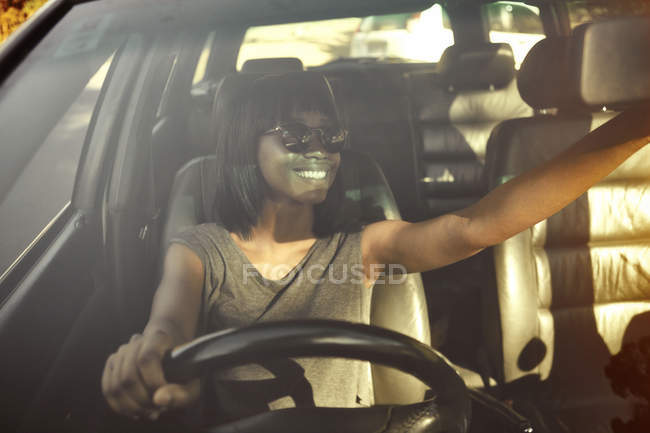 Mujer joven ajustando el espejo retrovisor en el coche, vista a través de la ventana del coche - foto de stock