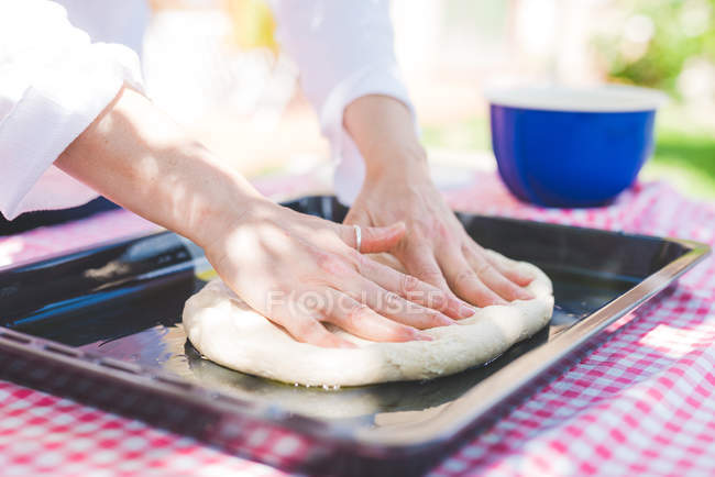 Imagen recortada de la mujer amasando masa en la bandeja para hornear en el jardín - foto de stock