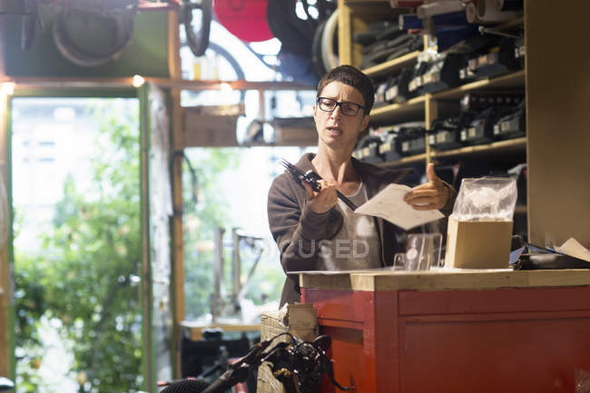 Woman at counter in bicycle workshop holding bike part and paperwork — Stock Photo