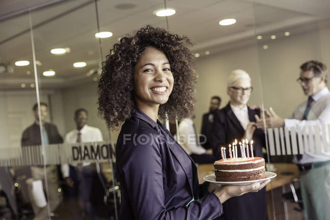 Giovane donna che presenta la torta con le candele al team di lavoro in sala riunioni — Foto stock