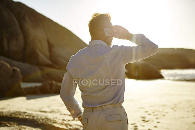 Зрілий чоловік стоїть на пляжі, користуючись смартфоном, заднім видом, Кейптаун, Південна Африка. — стокове фото