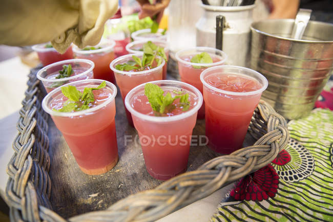 Stall holder garnishing fruit drinks with mint on cooperative food market stall — Stock Photo