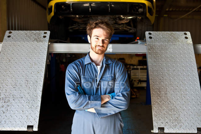 Portrait de mécanicien masculin derrière l'ascenseur de voiture dans le garage — Photo de stock