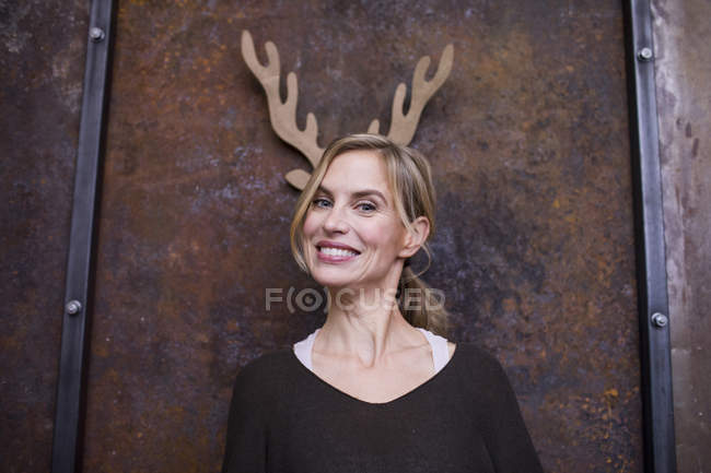 Portrait de femme adulte moyenne, souriante, bois de renne en carton sur le mur derrière elle — Photo de stock