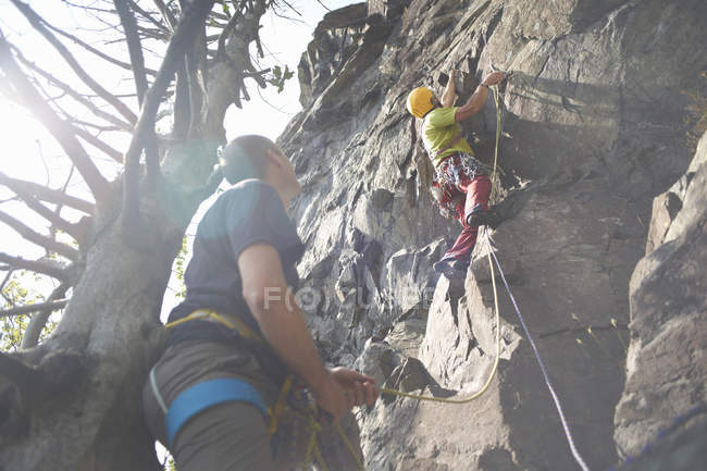 Low angle view of friends climbing rock face — Stock Photo