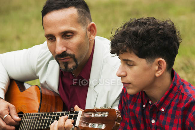 Отец и сын на улице, отец играет на гитаре — стоковое фото