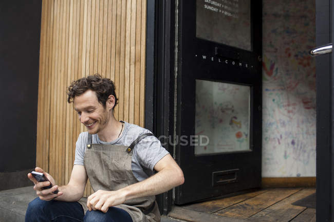Kellner macht Pause auf Café-Treppe und schaut aufs Smartphone — Stockfoto