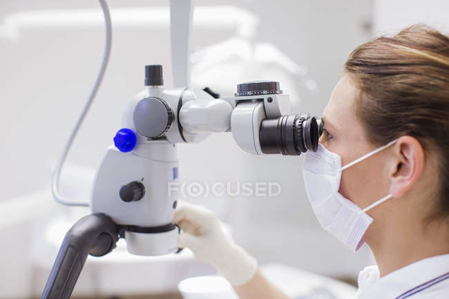 Vista lateral del dentista mirando a través del microscopio - foto de stock