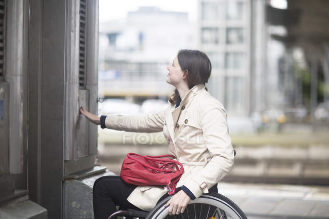 Young woman using wheelchair pressing control for city elevator — Stock Photo