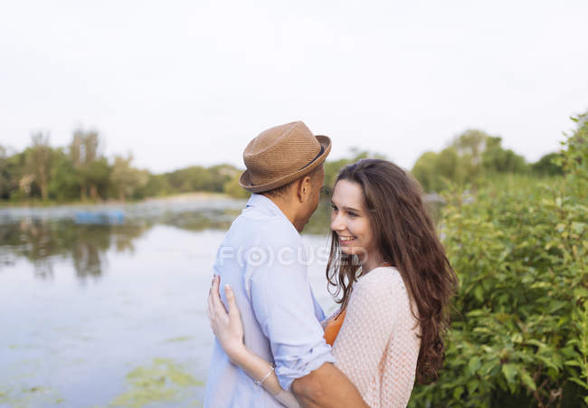 Vista lateral de pareja joven por el lago abrazos - foto de stock