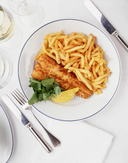 Fish and chips portion with lemon and green salad leaves, top view — Stock Photo