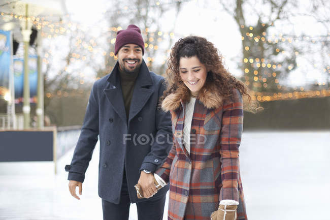 Couple sur la patinoire tenant les mains souriantes — Photo de stock
